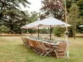 Table dressée pour un mariage jardin, avec des chaises en bois, des parasols et des guirlandes lumineuses.