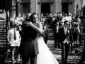 Un couple s'embrasse devant une église, entouré d'invités. Un jeune garçon tient un bouquet. Ce moment est le fruit d'un savant **rétroplanning mariage**.