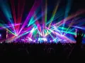 Une foule en délire sous un **totem jeux de lumière** spectaculaire, des faisceaux multicolores illuminent la scène et le public.