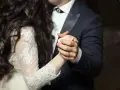 Les mains jointes d'un couple dansant une valse mariage. La mariée porte une robe en dentelle, le marié un costume sombre.