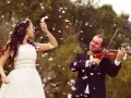 Une mariée en robe blanche danse sous une pluie de plumes, tandis que son mari joue du violon. Une scène féerique pour un mariage champêtre.