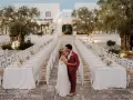 Un couple s'embrasse devant de longues tables dressées pour un mariage dans les Pouilles, illuminé par des guirlandes lumineuses.