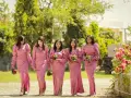 Cinq demoiselles d'honneur en robes roses marchent ensemble, tenant des bouquets.