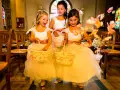 Trois enfants d'honneur souriantes, vêtues de robes claires, tiennent des paniers fleuris. Des pétales de roses volent autour d'elles dans une église.