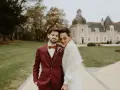 Un jeune marié rayonne dans son costume bordeaux, la couleur costume mariage parfaite pour un jour d'automne. Il enlace tendrement sa mariée devant un château.