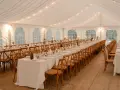 Ambiance chaleureuse sous tente pour un mariage, avec une longue table ronde ou rectangulaire dressée, éclairée par des guirlandes lumineuses et des bougies.