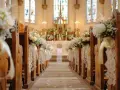 Allée d'église décorée pour un mariage. Des bouquets de fleurs et de la dentelle ornent les bancs, créant une ambiance romantique. Déco église mariage à faire soi-même.