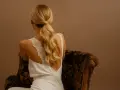 Une invitée de mariage arbore une élégante robe blanche et une queue de cheval blonde, assise sur un fauteuil fleuri.