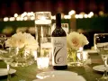 Bouteille de vin avec étiquette "Table 16", entourée de roses pâles, bougies et verres à vin. Parfait pour un dîner avec droit de bouchon traiteur.