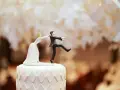 Figurines de mariés sur un gâteau. La mariée tire le marié par le revers. Un clin d'œil humoristique sur le prix d'un gâteau de mariage pour 100 personnes.