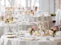 Un élégant plan de table mariage en U, avec des tables rondes dressées de vaisselle fine, de verres à pied, de bougies et de bouquets de roses.