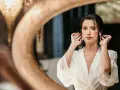 Une mariée, le visage marqué par le stress du mariage, ajuste ses boucles d'oreilles devant un miroir.