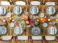 Plan de salle mariage table ronde : une table en bois dressée avec des assiettes fleuries, des verres en cristal, des fruits et des bouquets de fleurs.