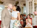 Un couple s'embrasse lors d'un mariage civil sans robe de mariée. La mariée porte un ensemble blanc moderne, le marié un costume beige.