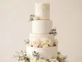 Magnifique gâteau de mariage traditionnel à quatre étages, orné de dentelle dorée, de roses pâles et de feuillage.