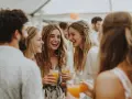Des jeunes femmes rient joyeusement lors d'une fête de mariage, un verre à la main. L'ambiance est festive, presque comme une "murder party mariage" où le suspense est remplacé par la joie.