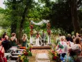 Un couple souriant lors d'une cérémonie laïque en plein air, entouré de verdure et de fleurs colorées. L'officiant cérémonie laïque guide ce moment unique.