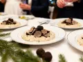 Un délicieux repas mariage hiver : des assiettes de risotto aux truffes noires, garnies de fines lamelles, sur une table dressée avec des branches de sapin.