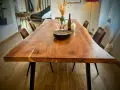 Table rectangulaire en bois massif, prête pour un repas festif dans une salle des fêtes. Assiettes décorées, verres et bouteille attendent les convives.