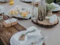 Table setting rustique pour une préparation de cérémonie laïque : assiettes, verres, plateau de fromages, cadeaux et décoration florale.