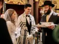 Un couple rayonne lors de leur mariage juif. Le marié, drapé d'un châle de prière, sourit à sa fiancée voilée. Un rabbin lit un document sacré.