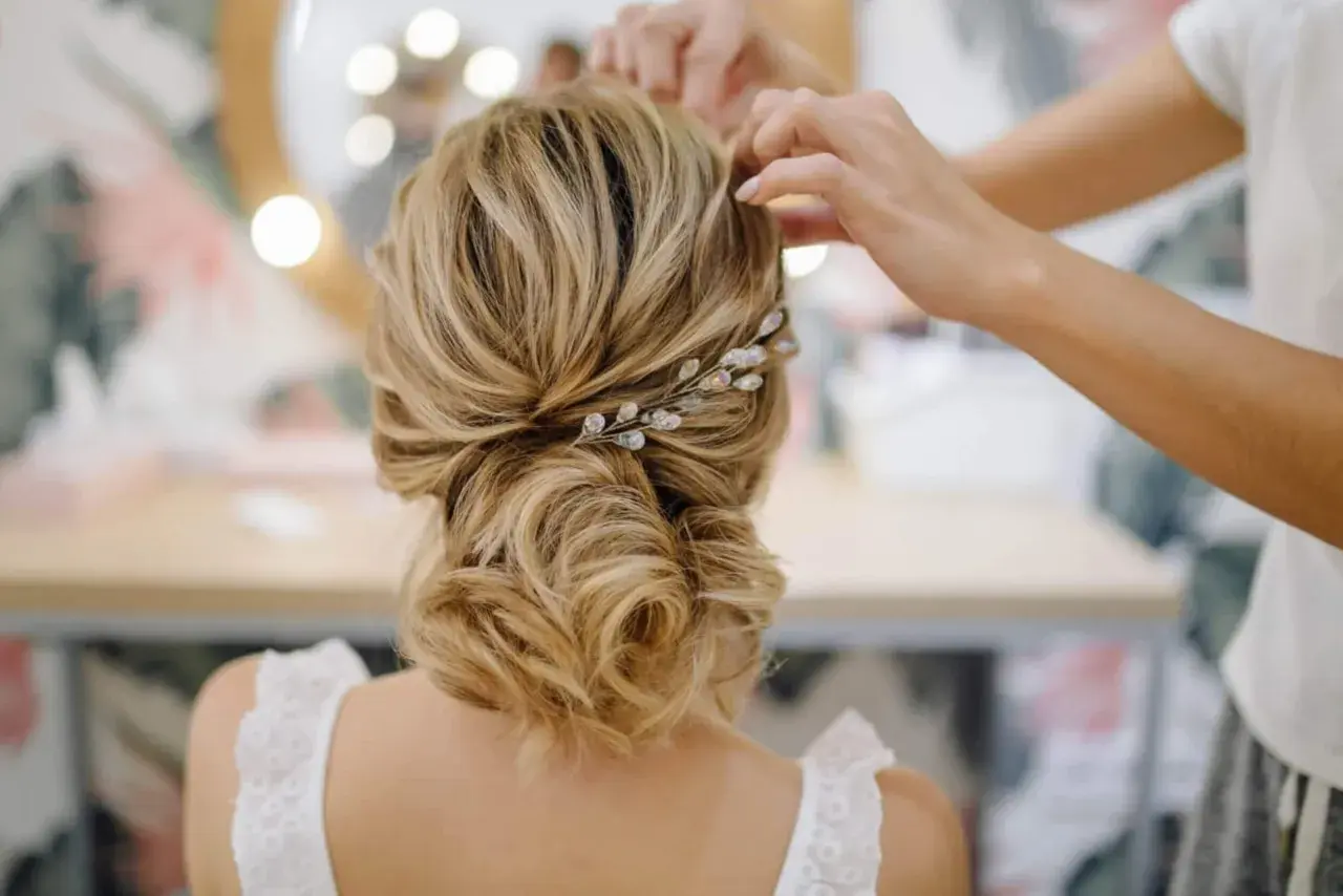 Une coiffure mariage chic avec un chignon flou orné d'une barrette scintillante. Les mains d'une coiffeuse ajustent les dernières mèches.