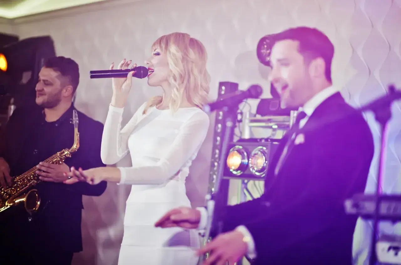 Un groupe de musique, dont une chanteuse en robe blanche, un saxophoniste et un chanteur en costume, anime une soirée.
