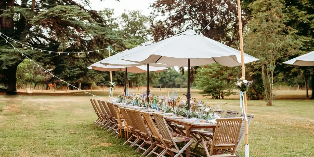 Table dressée pour un mariage jardin, avec des chaises en bois, des parasols et des guirlandes lumineuses.