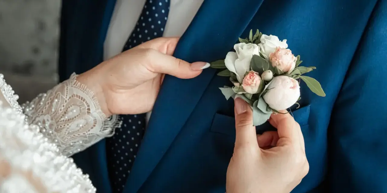 Les mains délicates de la mariée ajustent la boutonnière sur le costume bleu du marié, un symbole de leur mariage avec un étranger.
