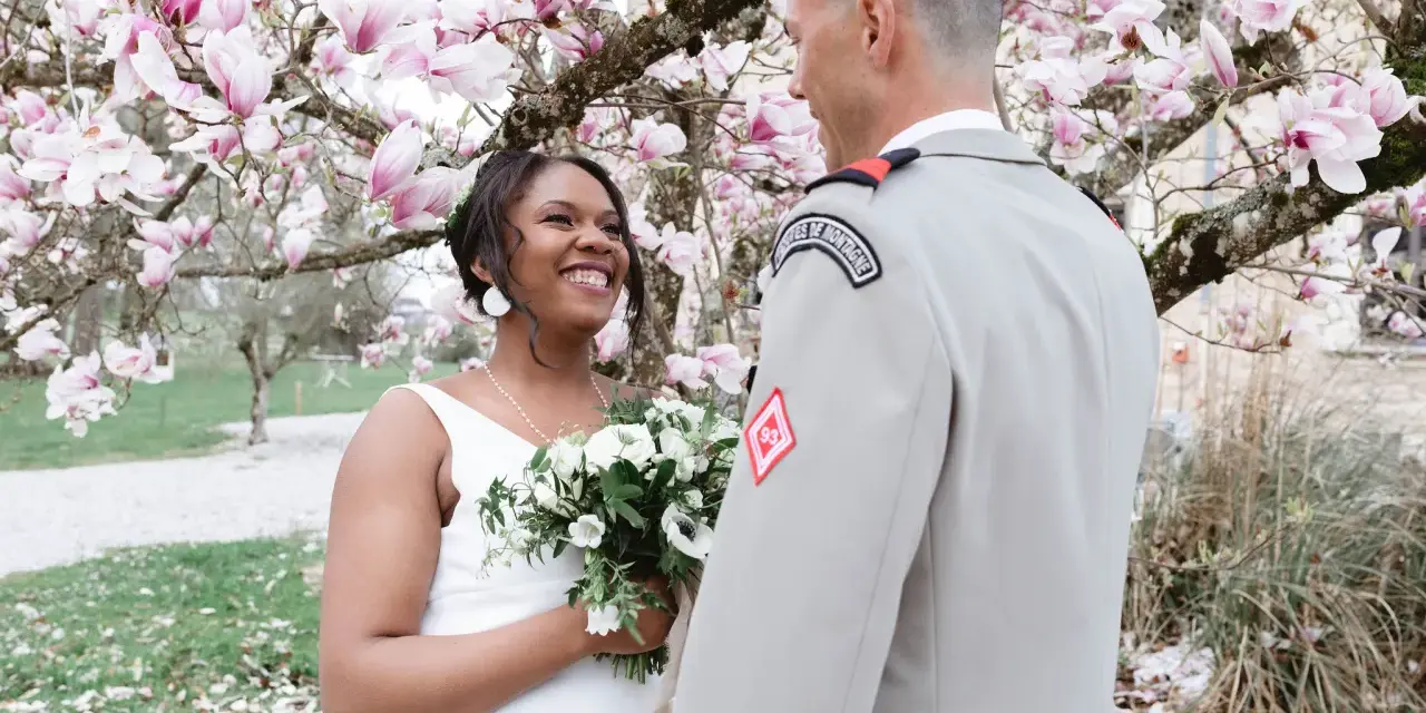 Un couple rayonnant lors de leur mariage militaire, sous un magnolia en fleurs.
