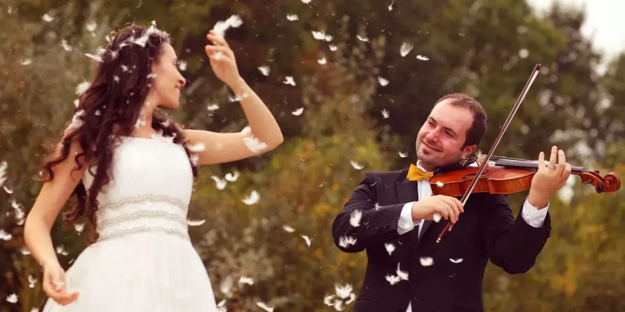 Une mariée en robe blanche danse sous une pluie de plumes, tandis que son mari joue du violon. Une scène féerique pour un mariage champêtre.