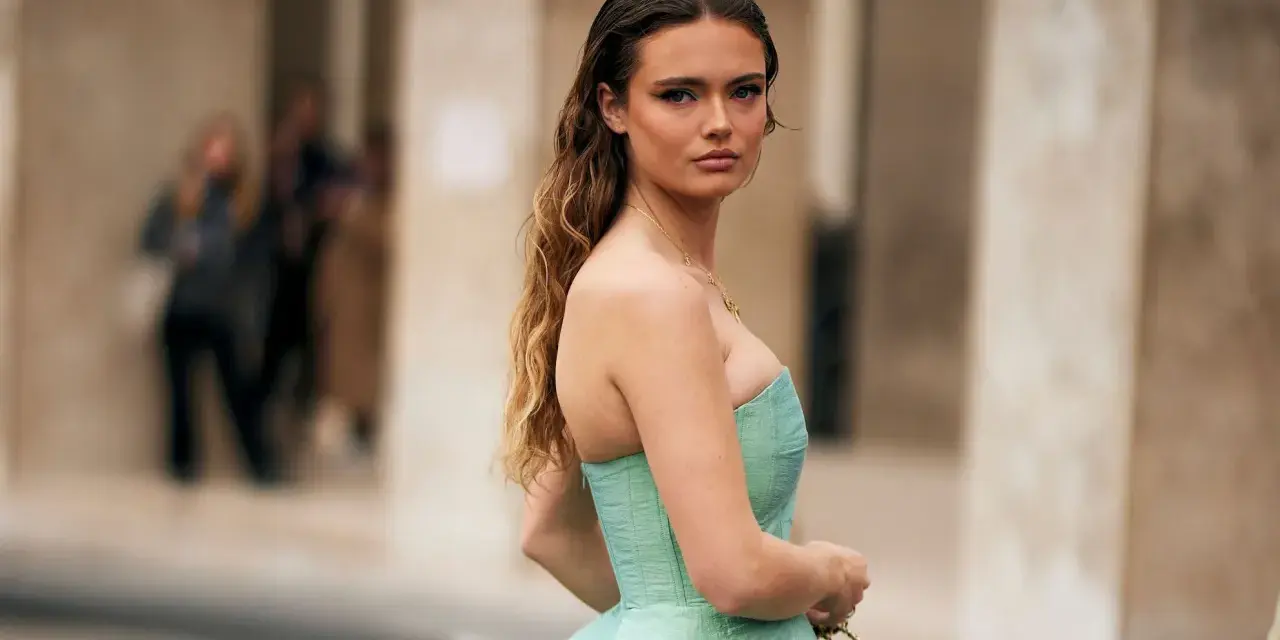 Une jeune femme en robe bustier vert menthe, parfaite pour savoir comment s'habiller pour un mariage. Cheveux longs ondulés, maquillage audacieux.