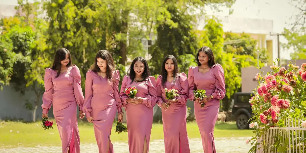 Cinq demoiselles d'honneur en robes roses marchent ensemble, tenant des bouquets.