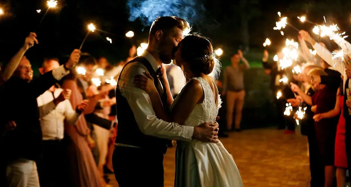 Un couple s'embrasse sous des feux de Bengale, entouré de leurs invités. Une belle idée d'animation mariage témoin pour un moment magique.