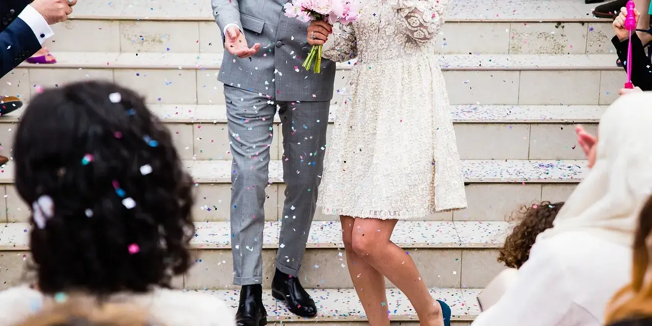 Un couple célèbre sa **danse mariage facile** sous une pluie de confettis. La mariée porte une robe blanche ornée, le marié un costume gris.