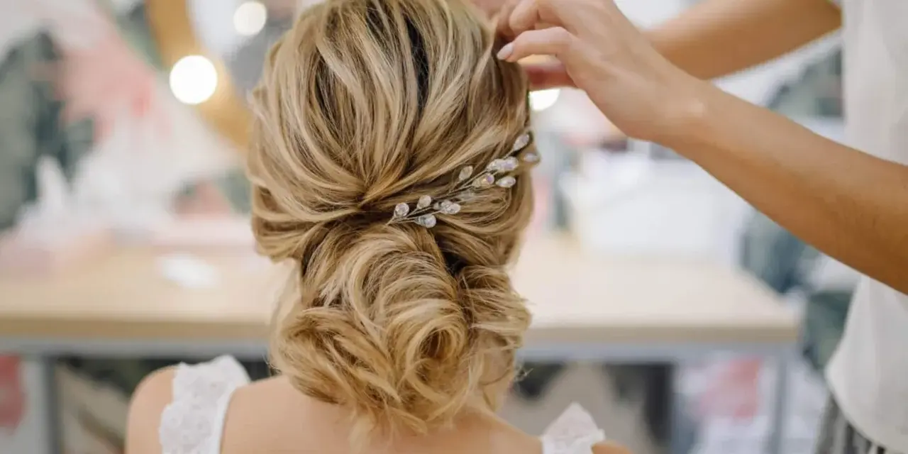 Une coiffure mariage chic avec un chignon flou orné d'une barrette scintillante. Les mains d'une coiffeuse ajustent les dernières mèches.