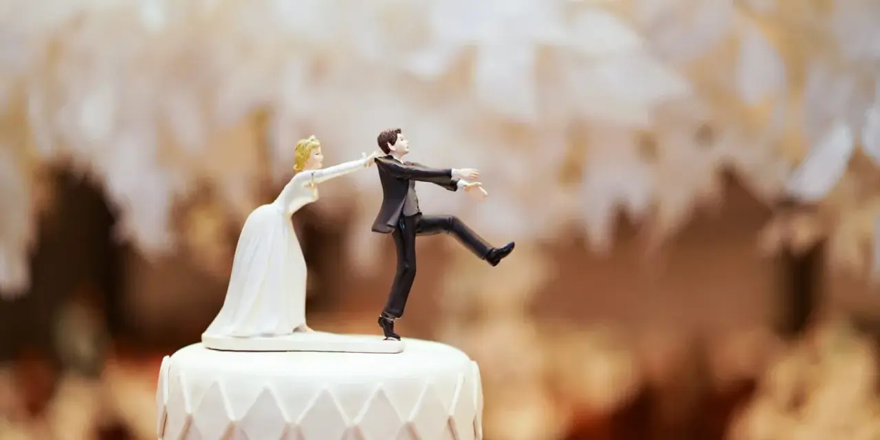 Figurines de mariés sur un gâteau. La mariée tire le marié par le revers. Un clin d'œil humoristique sur le prix d'un gâteau de mariage pour 100 personnes.