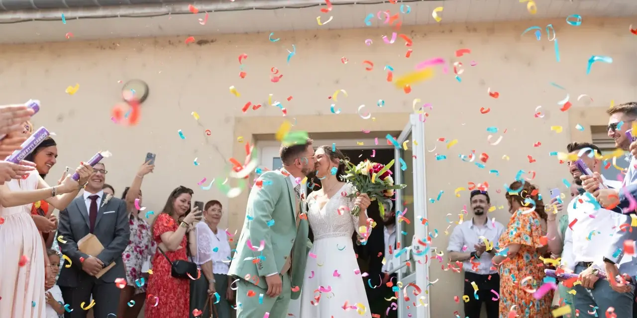Des confettis colorés pleuvent sur les jeunes mariés qui s'embrassent. Une joyeuse tradition pour célébrer leur union.