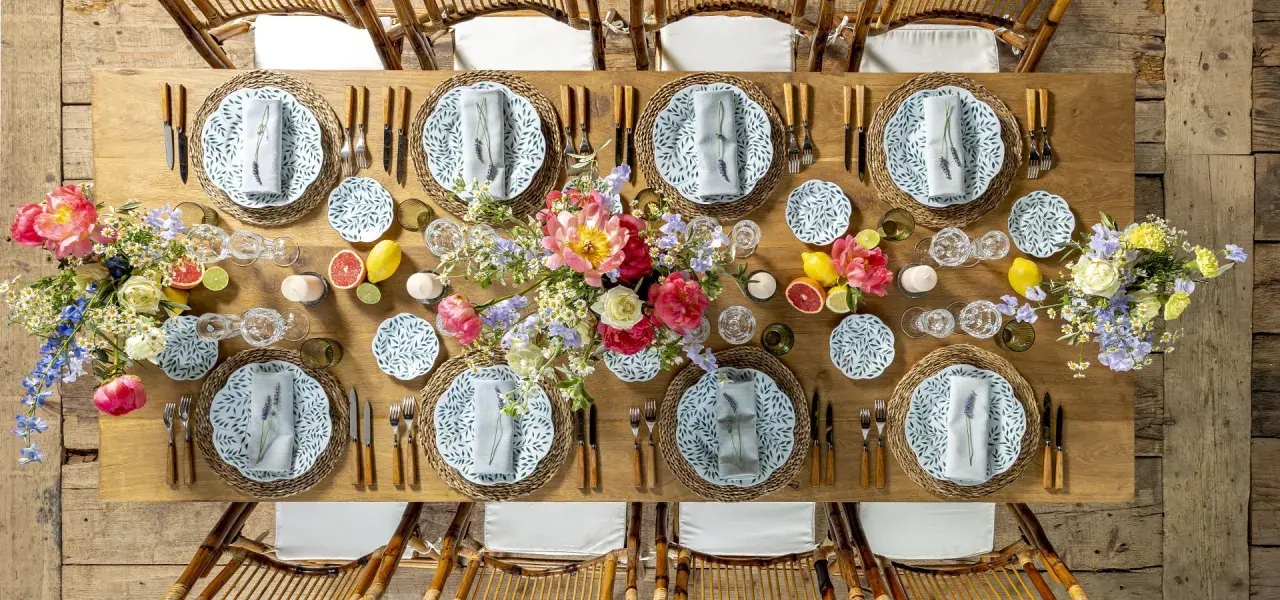 Plan de salle mariage table ronde : une table en bois dressée avec des assiettes fleuries, des verres en cristal, des fruits et des bouquets de fleurs.
