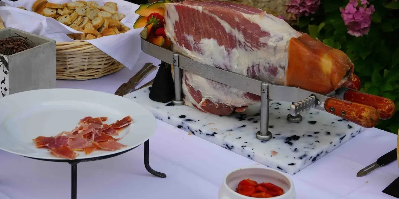 Un jambon cru entier prêt à être découpé, accompagné de pain et de fruits, pour un vin d'honneur original.