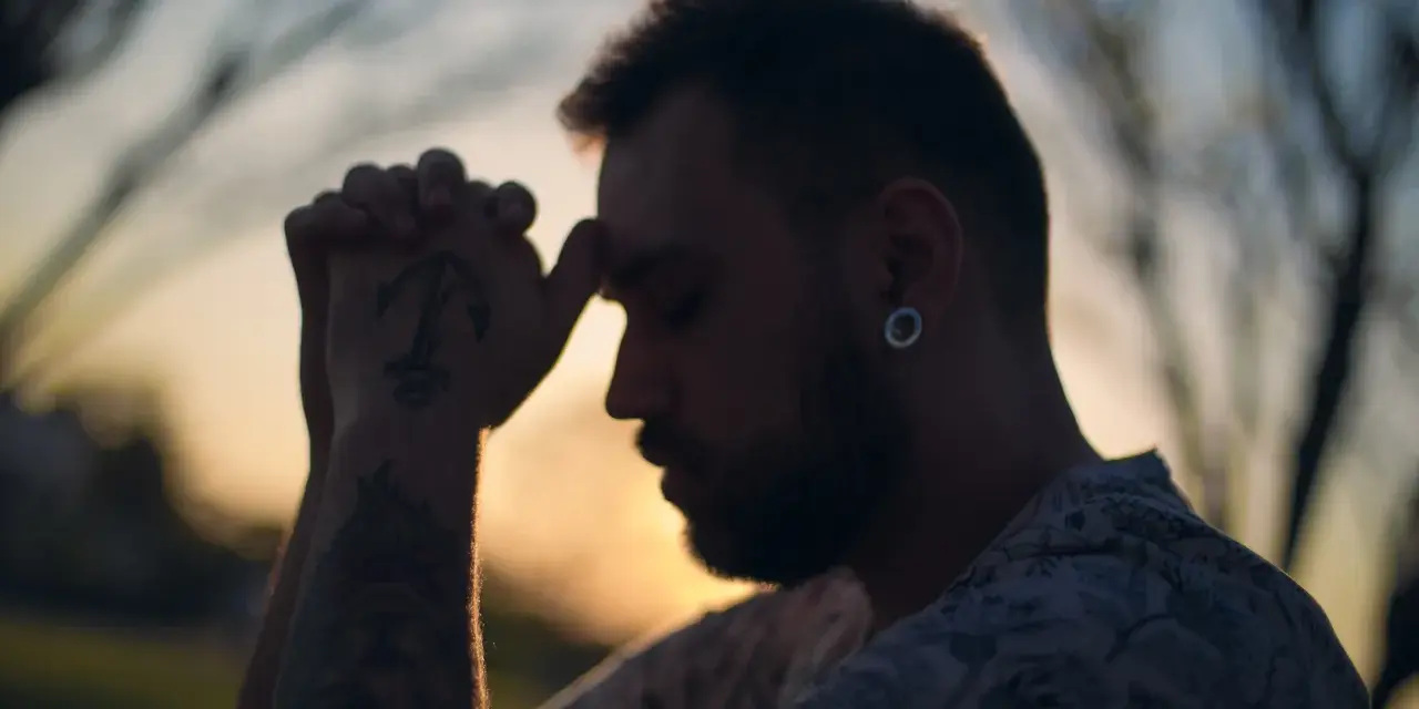 Un homme aux mains jointes, le front appuyé sur ses doigts, semble en pleine prière. Son tatouage d'ancre est visible. C'est un moment de prière des époux.