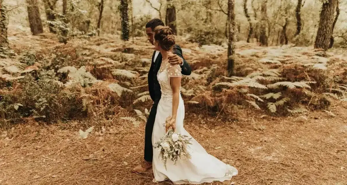 Un couple se promène dans une forêt, la mariée porte une robe blanche et tient un bouquet. Une scène de formalité mariage en pleine nature.