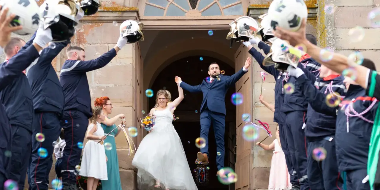 Mariés sortant de l'église sous une haie d'honneur mariage de pompiers lançant des bulles.