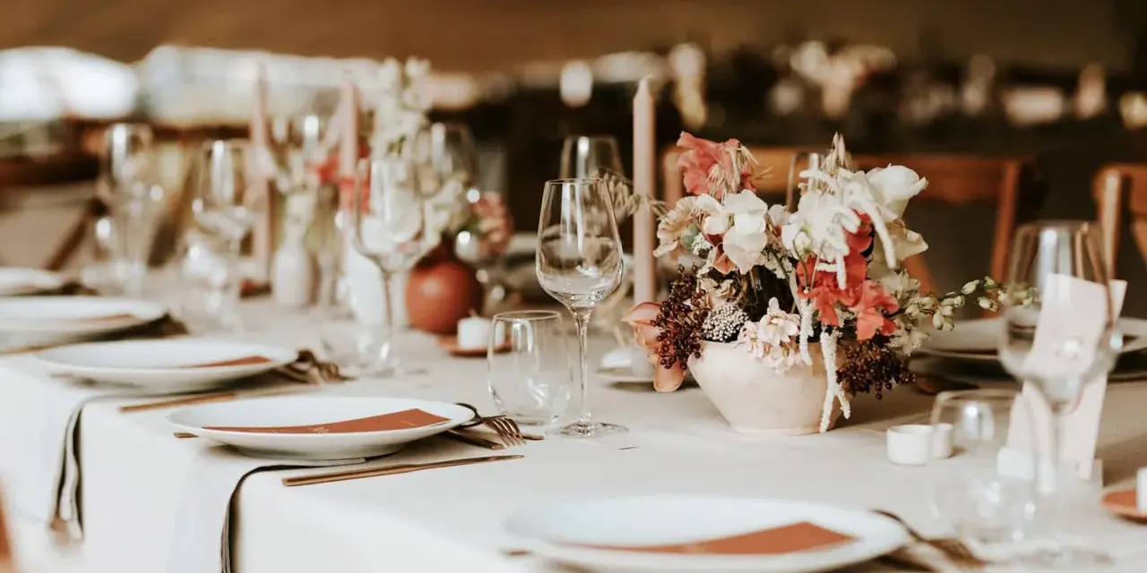 Un plan de table mariage élégant : vaisselle, verres, bougies et un bouquet de fleurs sur une table dressée.