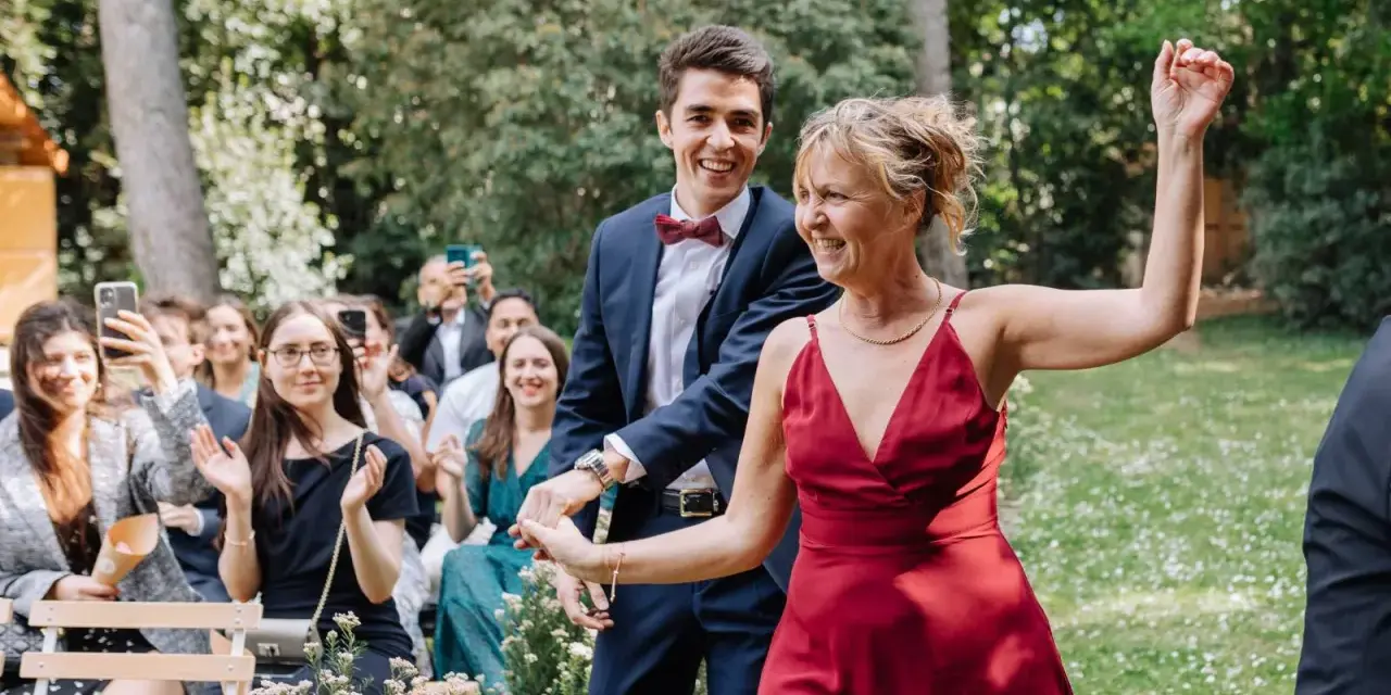 Un couple rayonnant danse lors d'un cortege mariage en plein air. La foule applaudit et filme ce moment joyeux.