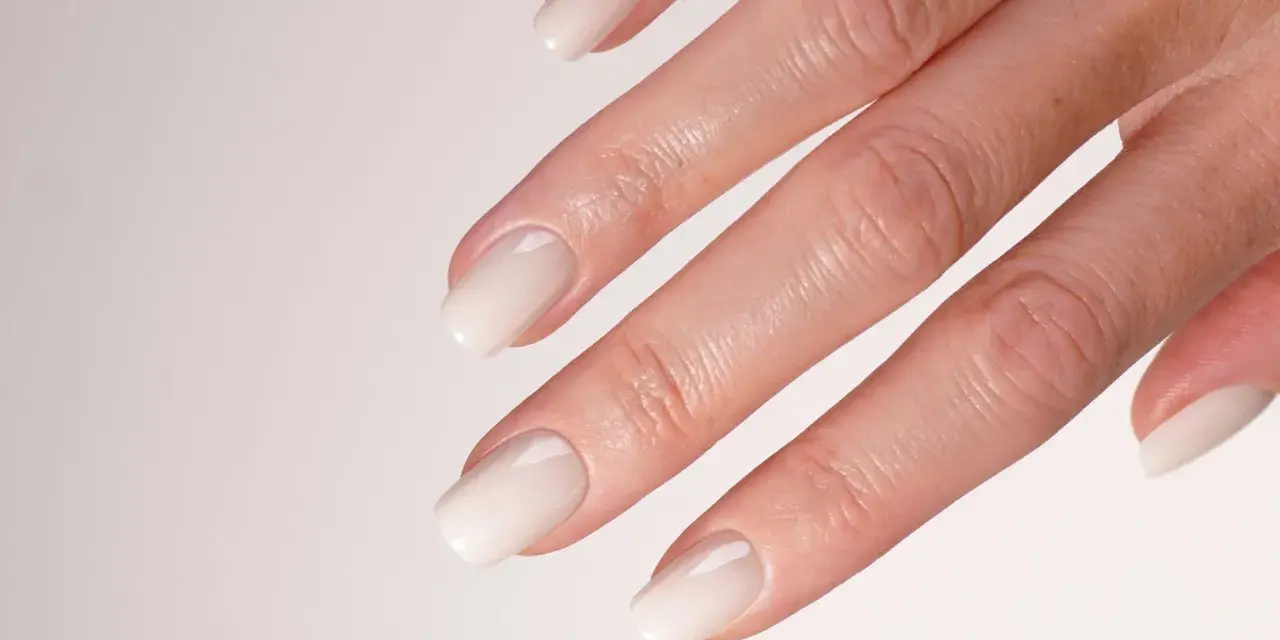 Main d'une mariée avec un french manucure spécial mariage, aux ongles laqués d'un blanc nacré, prêts pour le grand jour.
