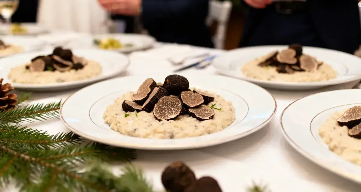 Un délicieux repas mariage hiver : des assiettes de risotto aux truffes noires, garnies de fines lamelles, sur une table dressée avec des branches de sapin.