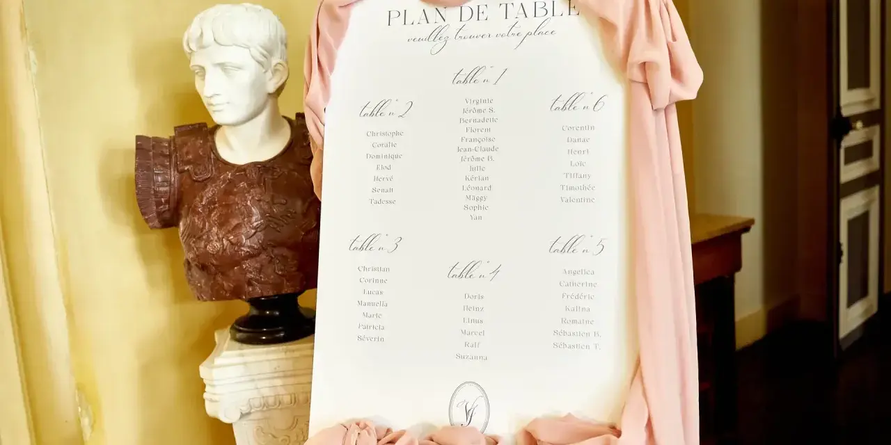 Plan de table de mariage, avec la disposition des invités par table. Une statue antique et des drapés roses décorent l'entrée.