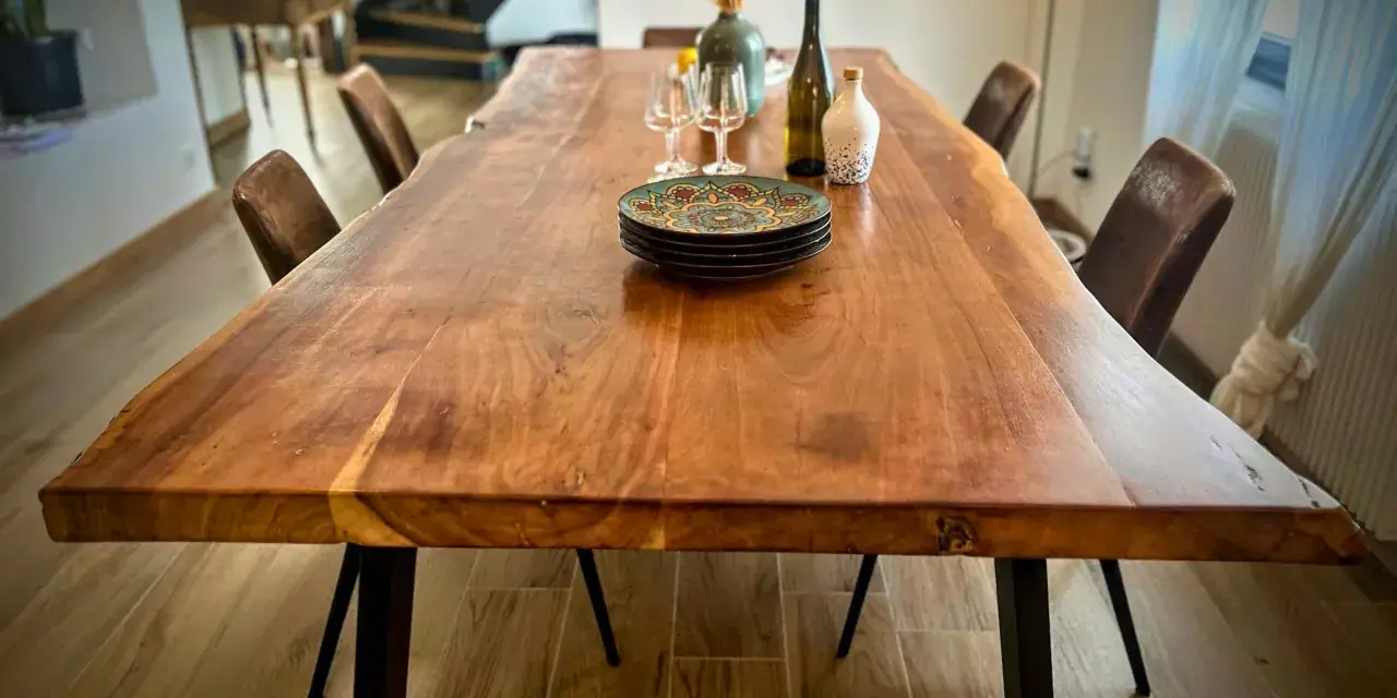 Table rectangulaire en bois massif, prête pour un repas festif dans une salle des fêtes. Assiettes décorées, verres et bouteille attendent les convives.