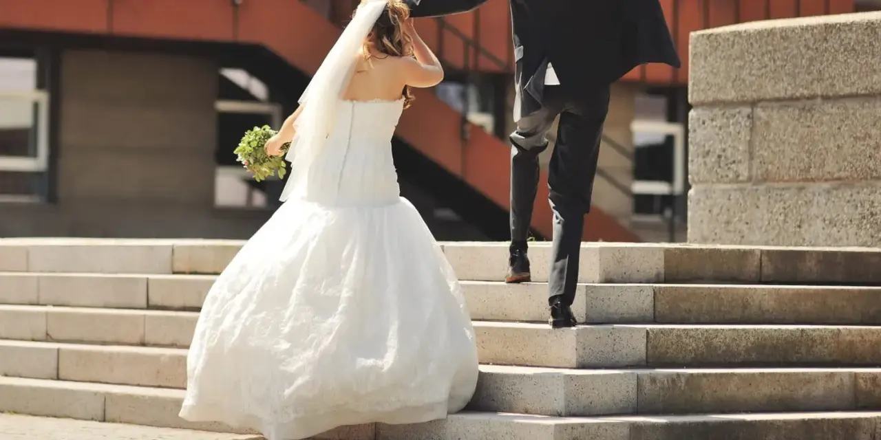 Un couple s'enfuit sur des escaliers après leur cérémonie de mariage. La mariée porte une robe blanche et un voile, tenant un bouquet.